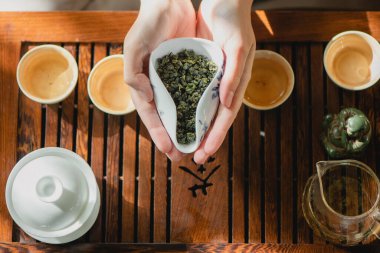 Dişilerin elinde kurumuş yeşil çay yapraklarıyla dolu bir fincan..