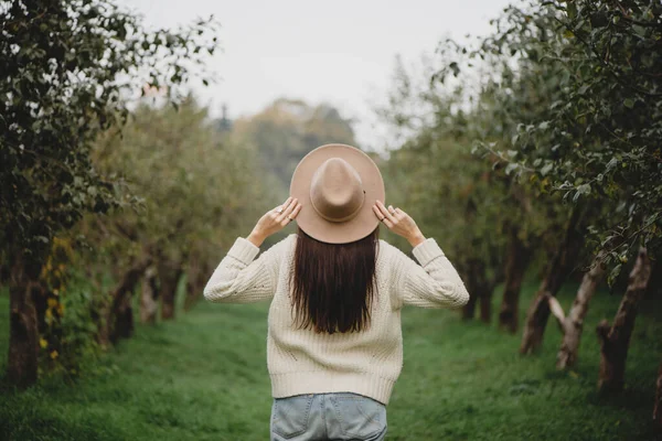 Stylische langhaarige Frau mit beigem Hut im Herbst-Obstgarten. — Stockfoto