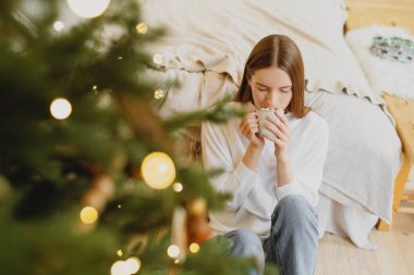 Genç ve güzel bir kadın Noel süslemeli evde lokumla sıcak çikolata içiyor..