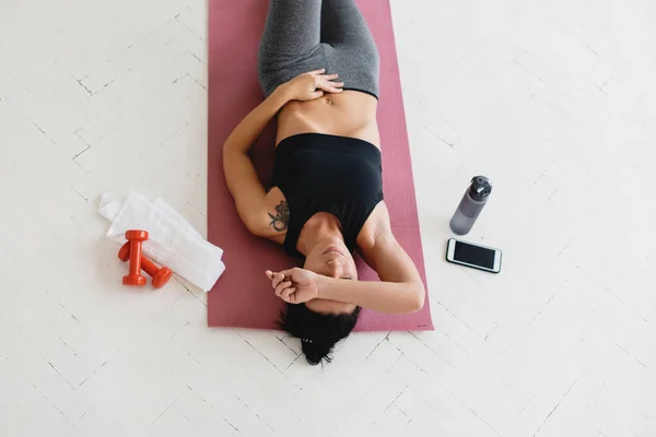 Mulher relaxante no tapete de fitness após o treino em casa. — Fotografia de Stock