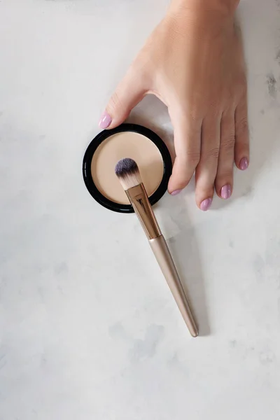 Female hand holding facial powder with brush.