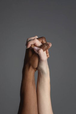 Gri arkaplanda birbirine kenetlenmiş beyaz ve siyah eller.