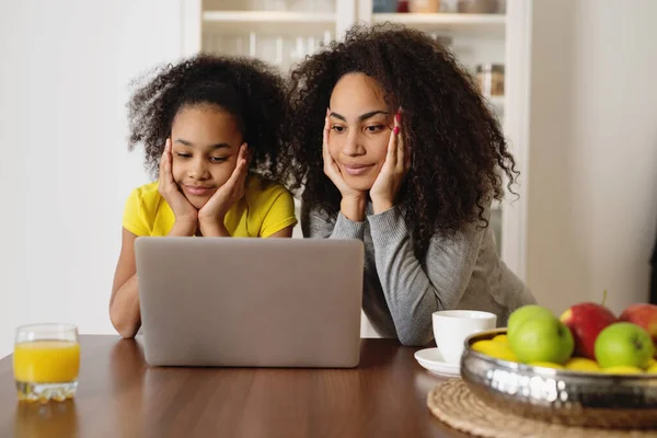 Afroamerikanische Mutter und Tochter sitzen in der Küche und benutzen Laptop. — Stockfoto