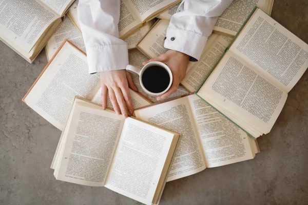 Kobiece ręce trzymające filiżankę kawy z książkami na tle. — Zdjęcie stockowe
