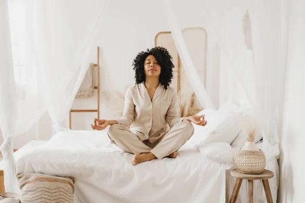 Mulher afro-americana atraente praticando exercícios de ioga e relaxamento na cama. — Fotografia de Stock