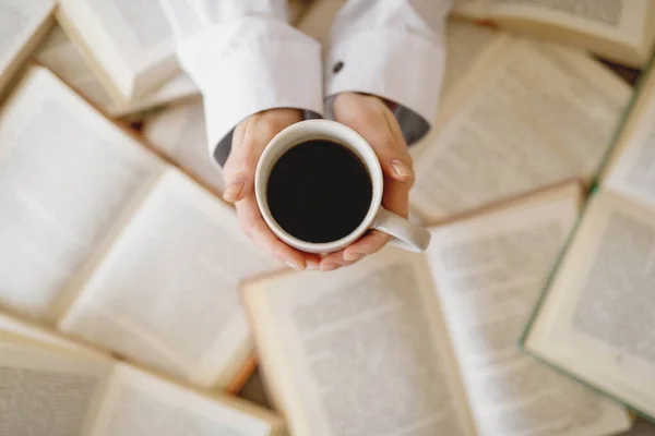 Widok z góry filiżanki kawy w rękach kobiety na tle otwartych książek. — Zdjęcie stockowe