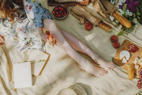 穿着白衣的年轻女子美丽的腿坐在毛毯上野餐. — 图库照片