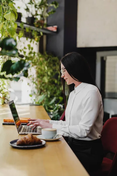 Seitenansicht einer erfolgreichen Geschäftsfrau mit Laptop in einem modernen Café. — Stockfoto