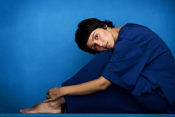 Jovem bela mulher sentada no fundo azul. — Fotografia de Stock