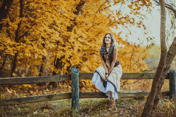 Young boho style woman in the autumn forest with a bouquet
