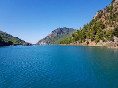 Güneşli, bulutsuz bir günde, dağların arka planına karşı deniz manzarası.