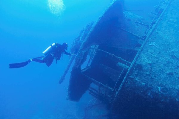 Человек ныряльщик с аквалангом, плавающий рядом с кораблём, разбился в синей глубокой воде. Крушение корабля SS Thistlegormm, Красное море Египет.