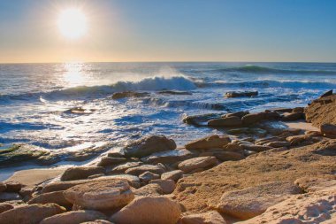 Colorful sunset viewed from the stony sea beach with soft waves