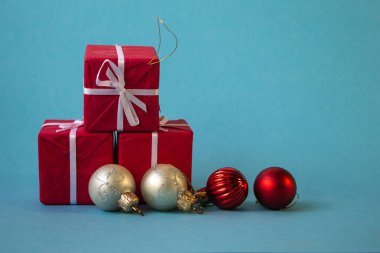 Üç kırmızı hediye kutusu ve mavi arka planda beyaz ve kırmızı Noel ağacı süslemeleri olan Noel afişi.