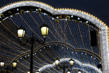 Akşam gökyüzünün arka planında ışık ve fener ışıklarından oluşan kemerli bir çelenk. Bayram bayrağı olarak.
