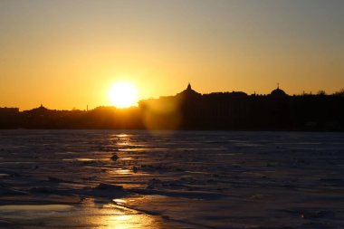View of the river from the quay to the ice drift during sunset with orange sun reflexes on the ice