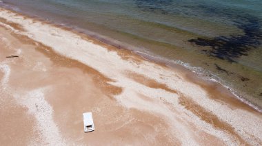Kumsalda beyaz bir şezlongla deniz ve sahil manzarası.