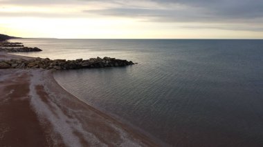 Sahil şeridinin havadan görünüşü, deniz ve su yüzeyi, turuncu günbatımı refleksleriyle doğal bir arka plan için ufukta.