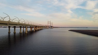 Kablolu köprü manzarası ve otoban gün batımında suyun üzerinde destekliyor. 