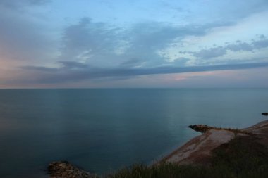 Yüksek sahilden deniz ve gökyüzüne gün batımı refleksiyle bak.