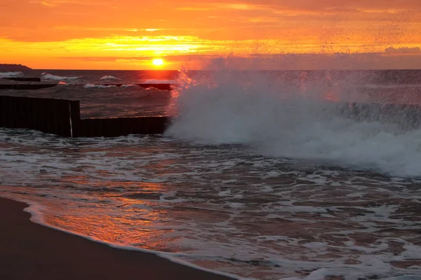 スプレーと海の泡に赤い反射と嵐の天気で海の上の美しい夕日 — ストック写真
