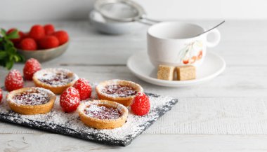 Ev yapımı bisküvi, üstünde ahududu reçeli kurabiye, kesme tahtasının üzerinde şeker tozu kaplı. Beyaz bir arkaplanda poz.