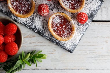 Ev yapımı bisküvi, üstünde ahududu reçeli kurabiye, kesme tahtasının üzerinde şeker tozu kaplı. Beyaz bir arkaplanda poz.