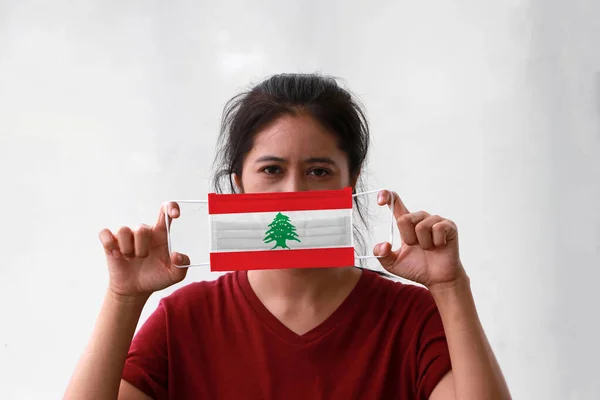 A woman and hygienic mask with Lebanon flag pattern in her hand and raises it to cover her face on white background. A mask is a very good protection from Tiny Particle or virus corona.