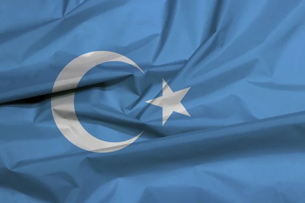 Doğu Türkistan 'ın kumaş bayrağı. Uyguristan bayrak arkaplan kırışıklığı, beyaz hilal ile mavi bir alan ve merkezin biraz solunda beş köşeli yıldız..