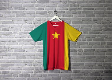 Gömlekte kamerun bayrağı, duvarda da tuğla desenli duvar kâğıdı, yeşil kırmızı ve sarı, altın yıldızlı..