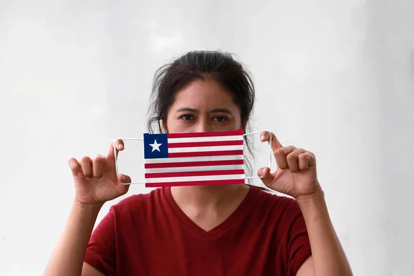 A woman and hygienic mask with Liberia flag pattern in her hand and raises it to cover her face on white background. A mask is a very good protection from Tiny Particle or respiratory disease.