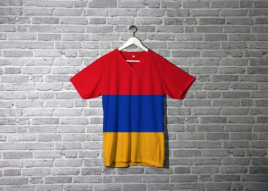 Tişörtünde Ermenistan bayrağı, duvarında da tuğla desenli duvar kağıdı, kırmızı mavi ve turuncu..