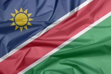Namibya 'nın kumaş bayrağı. Namibya bayraklı arka plan kırışıklığı, beyaz kenarlı kırmızı köşeli bant ve üçgen mavi, altın güneş ve alt üçgen yeşil..