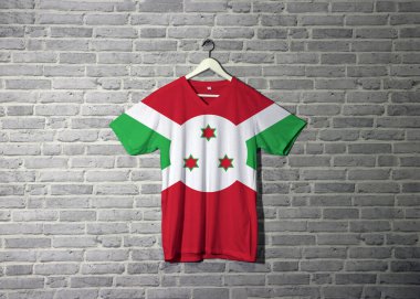 Gömlekte Burundi bayrağı, duvarda da da tuğla desenli duvar kâğıdı asılı. Beyaz köşegen haç kırmızı ve yeşil dört panele ve merkezdeki beyaz diskte üç yıldıza bölünür.. 