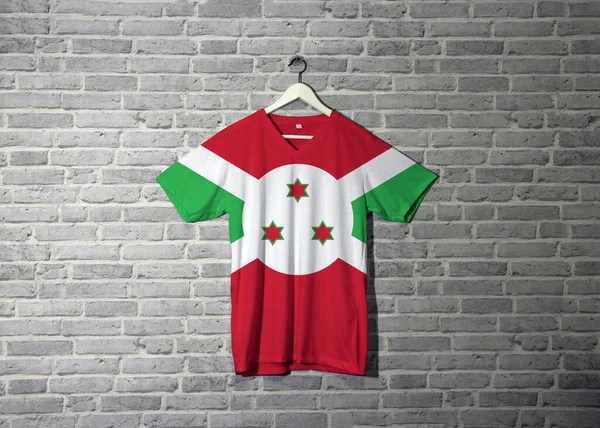 Gömlekte Burundi bayrağı, duvarda da da tuğla desenli duvar kâğıdı asılı. Beyaz köşegen haç kırmızı ve yeşil dört panele ve merkezdeki beyaz diskte üç yıldıza bölünür.. 