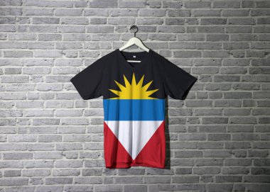 Antigua ve Barbuda bayrağı tişörtte ve duvarda tuğla desenli duvar kağıdıyla asılı. İki kırmızı üçgenli siyah ve beyaz yatay ve siyah üzerine sarı yarım güneş..