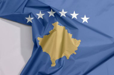 Kosova kumaşı, altı beyaz yıldızdan oluşan bir kavisle örtülmüş Kosova haritasıyla dolu mavi bir alan olan beyaz alanla krep ve buruşuyor.