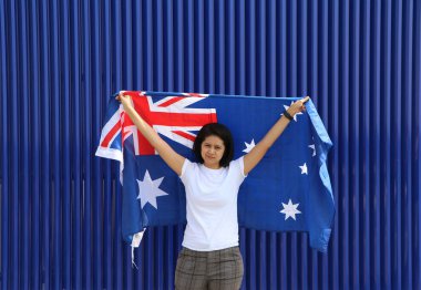 Güzel bayan elinde Avustralya bayrağını tutuyor ve mavi arka planda kolunun sonuna kadar kaldırıyor..