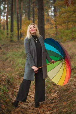 Sonbahar ceketli, sarışın ve parkta renkli şemsiyeli hoş bir kadın. Oldukça iri Avrupalı bir bayan.