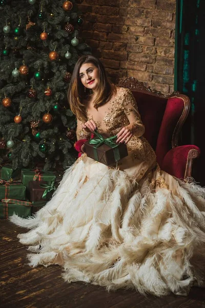 Christmas Holidays, Arabic woman in evening gorgeous dress. Pretty nice lady at Holly eve. Woman in beautiful golden sparkle dress with feathers
