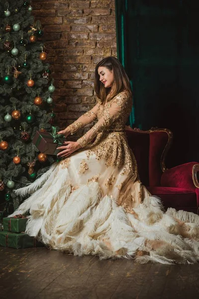 Christmas Holidays, Arabic woman in evening gorgeous dress. Pretty nice lady at Holly eve. Woman in beautiful golden sparkle dress with feathers