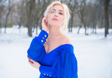 Kış tatili, kutlama ve insanlar konsepti - zarif mavi elbiseli, karlı orman arka planında seksi bir kadın