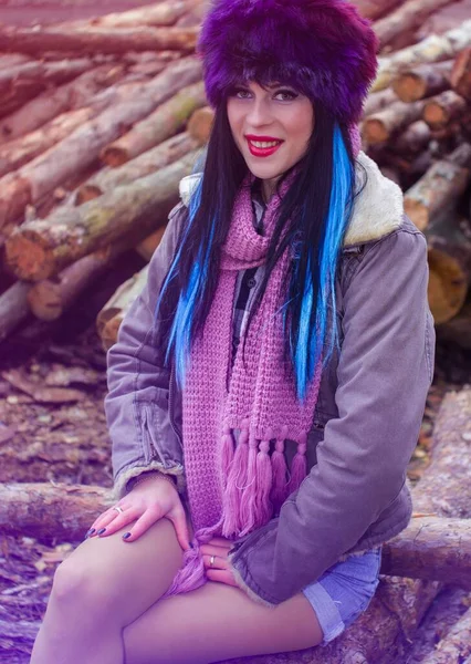 穿着假皮帽和夹克的现代美国风格的女人坐在森林里 一个有着长发和明亮假日的年轻女子在锯木厂化妆 — 图库照片
