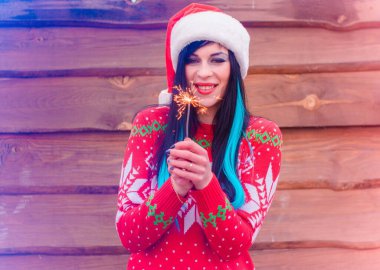 Mavi saçlı, örgü Noel süveteri ve ahşap arka planda şapkası olan hoş bir kız Bengal ışıkları tutuyor ve yeni yıl ve Noel için mutlu. Kış Tatillerinin Mucizeleri ve Mutlulukları