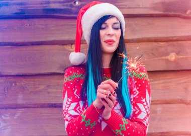 Mavi saçlı, örgü Noel süveteri ve ahşap arka planda şapkası olan hoş bir kız Bengal ışıkları tutuyor ve yeni yıl ve Noel için mutlu. Kış Tatillerinin Mucizeleri ve Mutlulukları