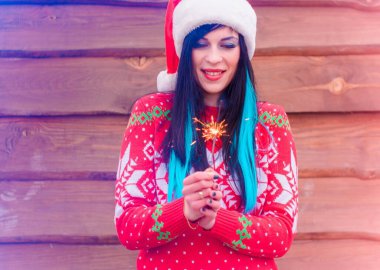 Mavi saçlı, örgü Noel süveteri ve ahşap arka planda şapkası olan hoş bir kız Bengal ışıkları tutuyor ve yeni yıl ve Noel için mutlu. Kış Tatillerinin Mucizeleri ve Mutlulukları