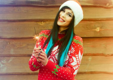 Mavi saçlı, örgü Noel süveteri ve ahşap arka planda şapkası olan hoş bir kız Bengal ışıkları tutuyor ve yeni yıl ve Noel için mutlu. Kış Tatillerinin Mucizeleri ve Mutlulukları