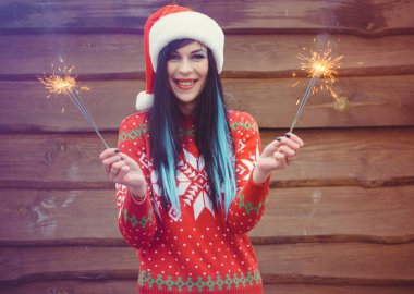 Mavi saçlı, örgü Noel süveteri ve ahşap arka planda şapkası olan hoş bir kız Bengal ışıkları tutuyor ve yeni yıl ve Noel için mutlu. Kış Tatillerinin Mucizeleri ve Mutlulukları