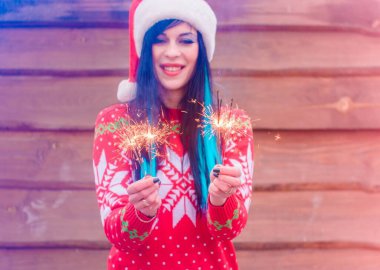 Mavi saçlı, örgü Noel süveteri ve ahşap arka planda şapkası olan hoş bir kız Bengal ışıkları tutuyor ve yeni yıl ve Noel için mutlu. Kış Tatillerinin Mucizeleri ve Mutlulukları