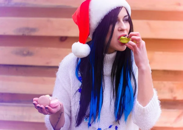 Nice young woman in the New Year\'s cap actively eats sweets and cookies. Rationing sweet in the New Year and Christmas holidays, girls and diet. Harm of sugar on the human body, joy in everyday life